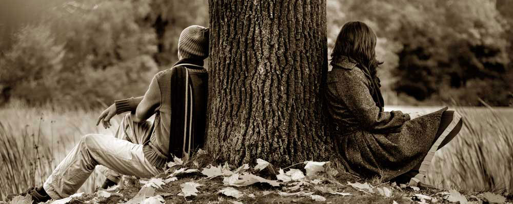 Zwei Personen sitzen getrennt an Baum, Herbststimmung.